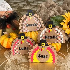 three turkey place cards sitting on top of a table next to sunflowers and pumpkins