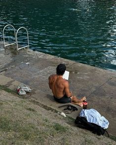 a shirtless man sitting on the edge of a body of water with his laptop