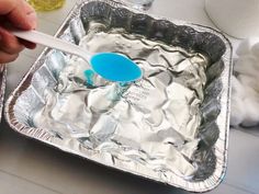 a person holding a spoon in an aluminum pan with ice cubes on the side