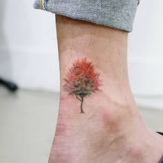 a small tree tattoo on the ankle that is red and green with leaves in it