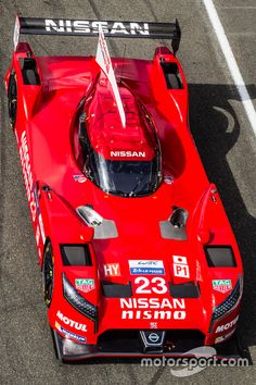 a red race car driving on a track with the number 23 nissan written on it