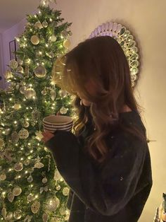 a woman standing in front of a christmas tree holding a plate and looking at it