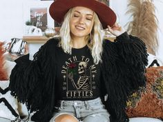 a woman sitting on a couch wearing a black shirt with fringe sleeves and a red hat