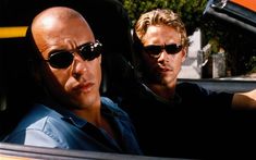 two men sitting in the back seat of a car, one with sunglasses on his head