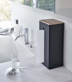 a bathroom sink with a paper towel dispenser next to it and a glass of water on the counter