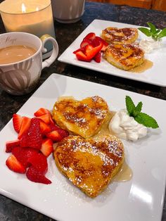 two white plates topped with heart shaped pancakes and strawberries next to a cup of coffee