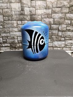 a black and white fish painted on a blue jar sitting on top of a table