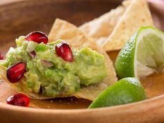 guacamole with pomegranate and limes in a wooden bowl