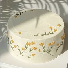 a white cake with yellow flowers painted on it's side sitting on a table