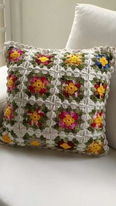 a crocheted pillow sitting on top of a white couch next to a window