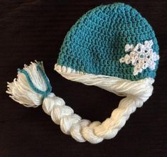 a crocheted hat with white and blue flowers on it sitting on a table