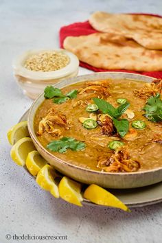 a bowl of food on a plate with lemons and pita bread in the background