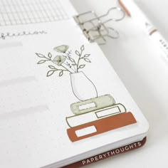 an open notebook with a drawing of a flower in a vase on top of it