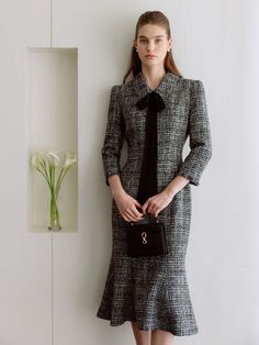 a woman standing next to a wall holding a black and white purse in her hand