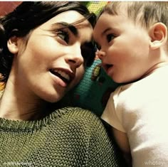 a woman laying next to a baby on top of a couch with her face close to the child's head