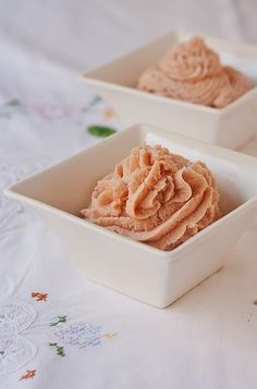 two small white bowls filled with food on top of a tablecloth covered table cloth