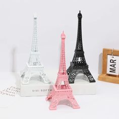 three miniature eiffel tower models are displayed on a white surface, one is pink and the other is black