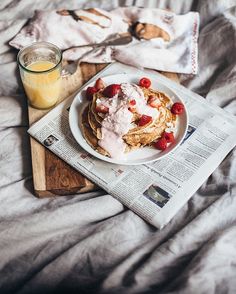 a plate of pancakes with whipped cream and strawberries next to a glass of orange juice