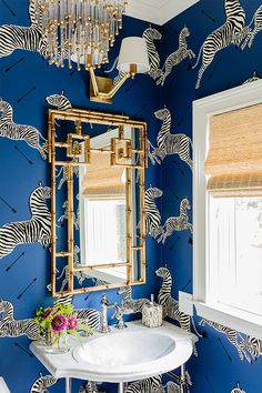 a blue bathroom with zebra wallpaper and gold accents on the mirror above the sink