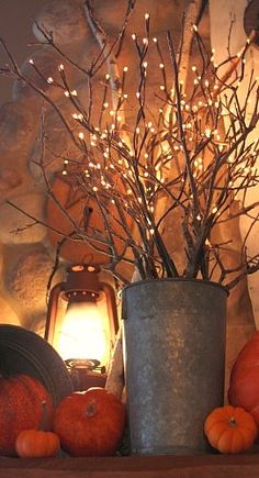 an arrangement of pumpkins and branches on a mantel with a lantern in the background