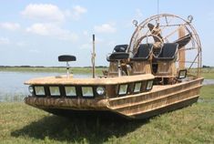 a large wooden boat sitting on top of a lush green field next to a lake