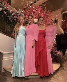 four women in long dresses standing next to each other on a staircase with pink flowers