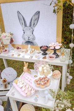 a table topped with cakes and pastries next to a bunny painting on the wall