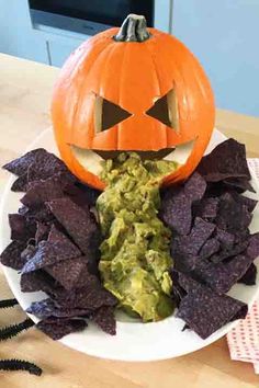 a white plate topped with guacamole chips and a jack o lantern pumpkin