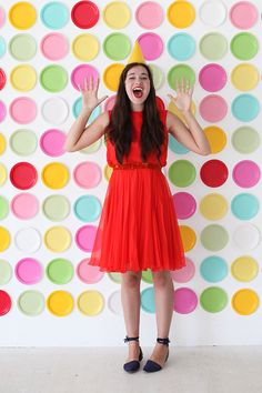 a woman wearing a red dress and black shoes standing in front of a polka dot wall