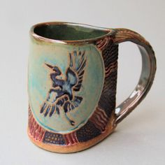 a blue and brown mug with a bird painted on it's side, sitting on a white surface