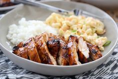 a white bowl filled with meat and rice next to a fork on a tablecloth