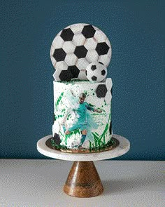 a soccer themed cake on a stand with a soccer ball topper and green grass