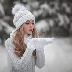 a woman blowing snow with her hands in front of her face and wearing a white hat