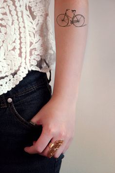 a woman with a bike tattoo on her left arm is wearing jeans and a white top