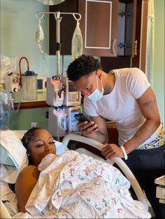 a man standing next to a woman in a hospital bed looking at a cell phone