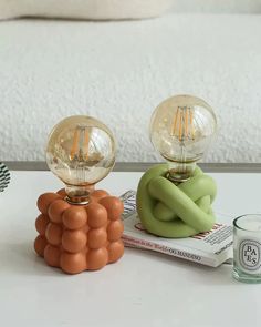 two lamps sitting on top of a table next to a glass cup and candle holder