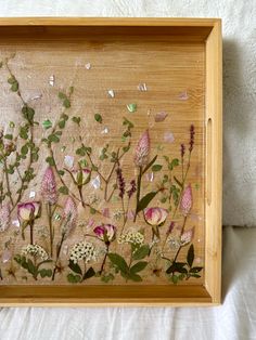 a wooden frame with pressed flowers and leaves on the inside, sitting on a bed