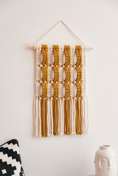 a wall hanging made out of macrame beads and tassels on a white wall