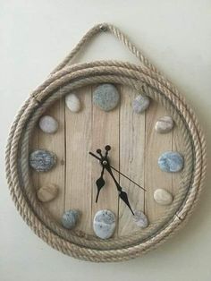 a clock made out of wood and rope with rocks on the sides, hanging from a wall