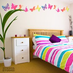 a bed room with a neatly made bed next to a potted plant and wall decals