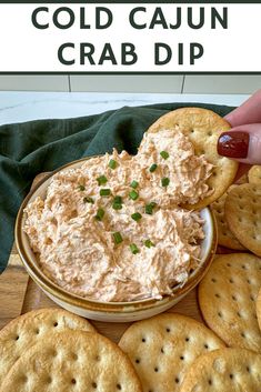 a cracker being dipped into a bowl of cold cajun crab dip surrounded by crackers