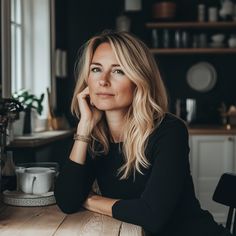 a woman sitting at a wooden table with her hand on her chin and looking off into the distance