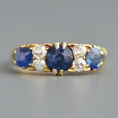 A beautiful antique Victorian period (1837-1901) sapphire and old mine cut diamond half hoop ring in 18k yellow gold. This wonderful and classic Victorian period sapphire and diamond ring features three natural rich blue sapphires prong set with four sparkling white old mine cut diamonds spaced in between all above a highly detailed carved and pierced lower gallery that is curved to hug the finger and leads to equally fanciful carved shoulders and a smooth rear band. Fully hallmarked for London, Antique Blue Diamond Ring With Rose Cut, Vintage Blue Diamond Ring With Single Cut Diamonds, Vintage Blue Single Cut Diamond Rings, Vintage Blue Ring With Single Cut Diamonds, Vintage Blue Rings With Single Cut Diamonds, Grad Presents, Antique Engagement Rings Sapphire, Antique Gold Rings, Old Mine Cut Diamond