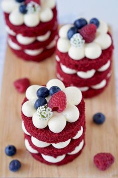 red velvet cakes with white frosting and blueberries on a wooden board next to raspberries