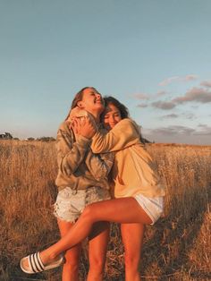 two girls are hugging in the middle of a field with tall grass and blue sky