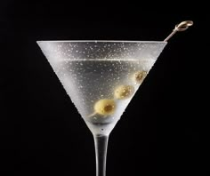 a martini glass with olives in it on a black background and water droplets falling from the rim