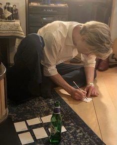 a man sitting on the floor writing in front of a bottle of alcohol and papers