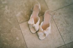 a pair of white shoes with bows on them sitting on the floor in front of a tile floor