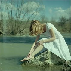 a woman sitting on top of a rock in the water