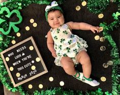 a baby laying on top of a black mat covered in green grass and shamrock decorations